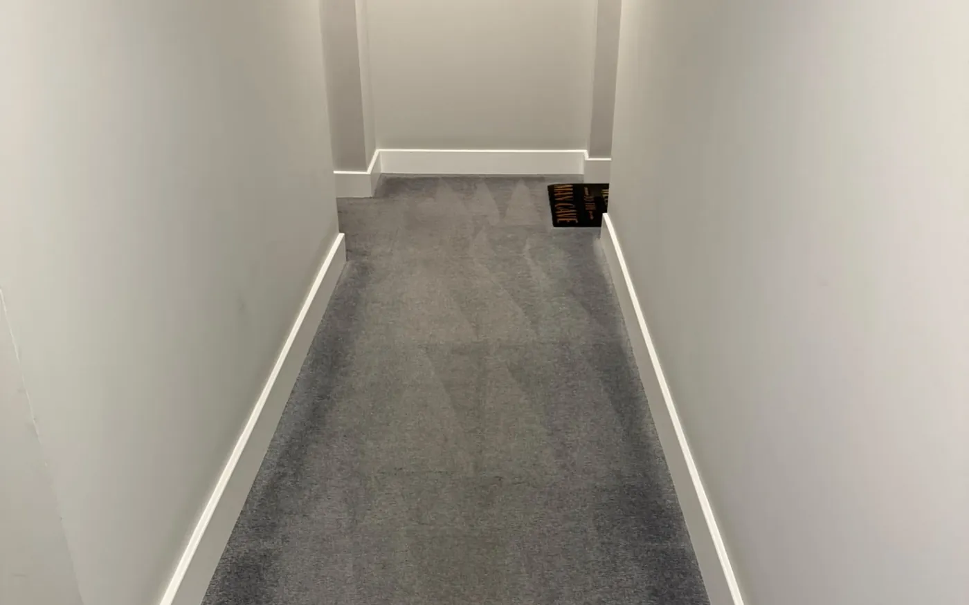 Long communal corridor in a London residential block, carpet cleaned end to end, entrance matting at the far door
