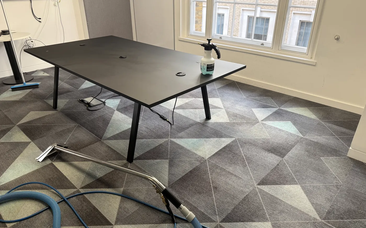 Extraction wand and hose on patterned carpet tiles in a London meeting room, pre-spray on the table